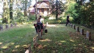 Vier Jungs auf einer Kriegsgräberstätte, einzelne von ihnen beugen sich über einen Grabstein und säubern ihn