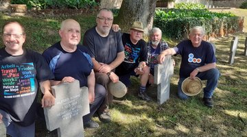 Sechs Männer knien neben Grabkreuzen