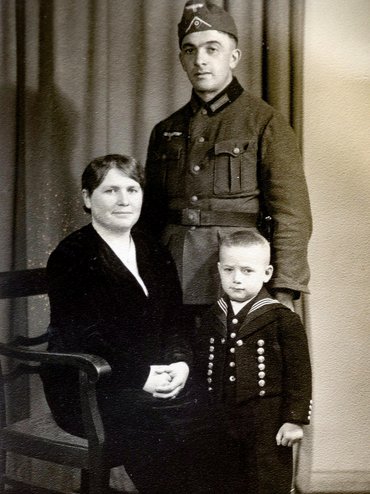 Familienporträt in schwarz-weiß: Soldat in Uniform, Mutter sitzend und kleiner Sohn daneben.