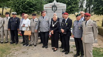 Eine Gruppe von ca. 15 Personen, teilweise in Uniform oder Anzug, vor einem Kriegerdenkmal