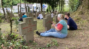 Mehrere Personen sitzen vor Kriegsgräbern und ziehen die Schrift mit einem Stift nach